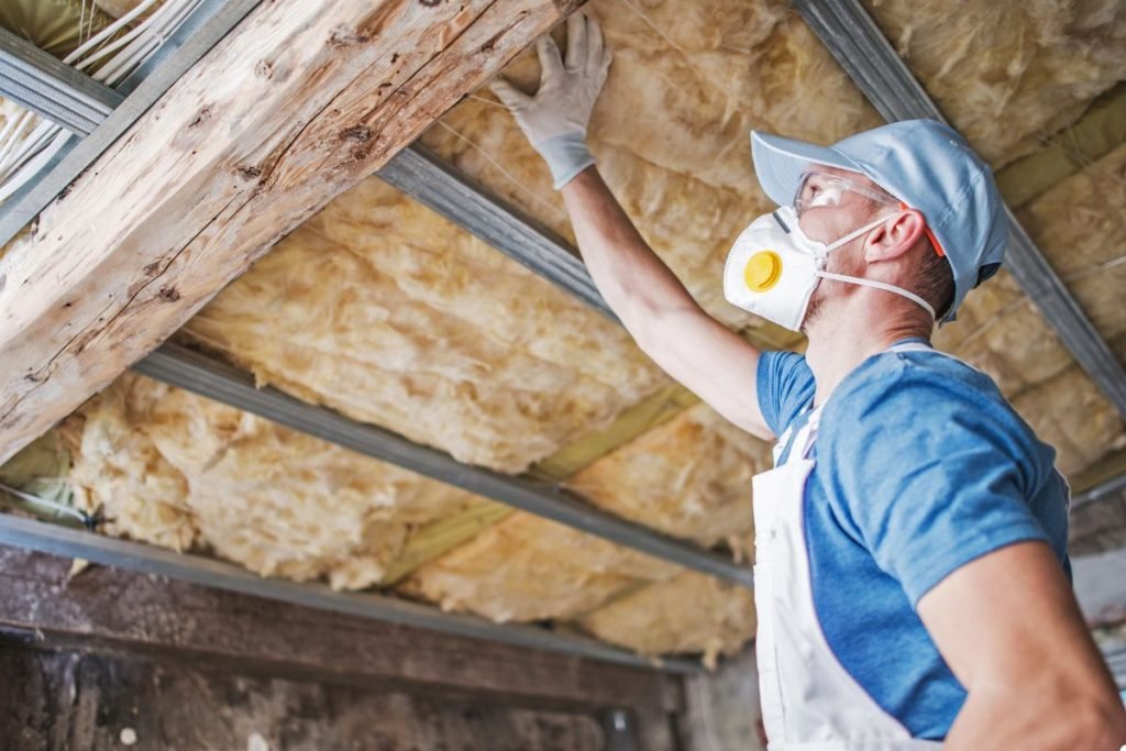 A man in a mask and gloves is repairing a ceiling, focused on his work with tools in hand.