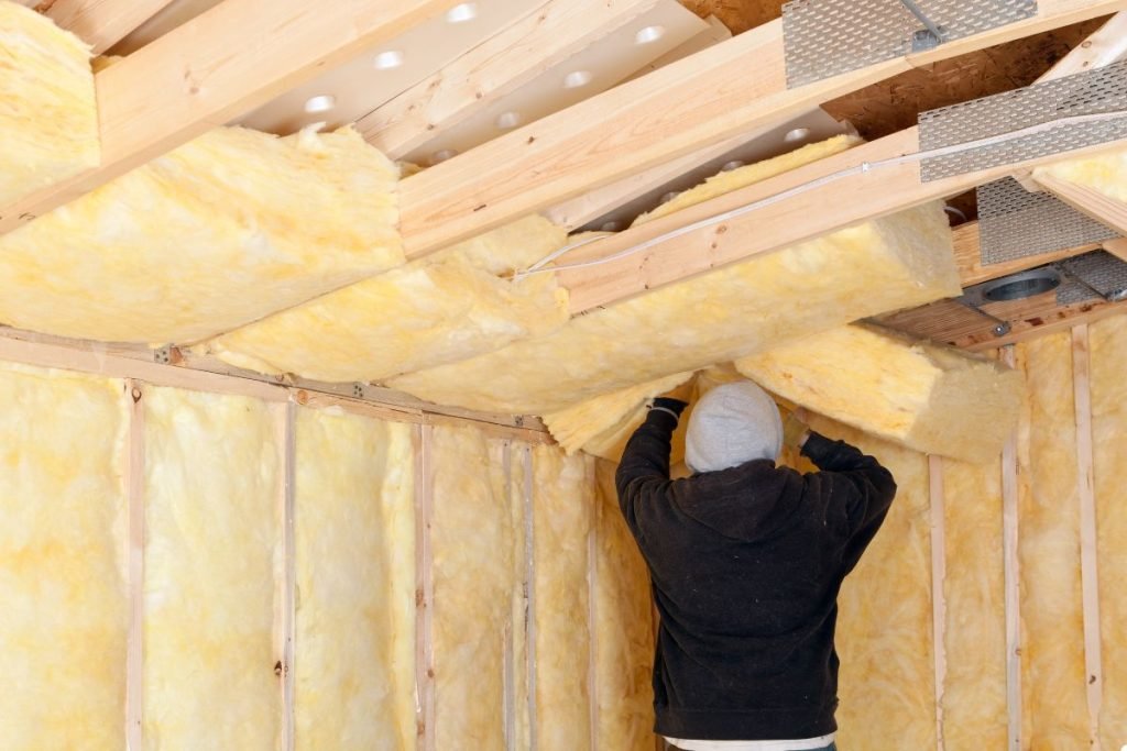 A man installs insulation in a room, carefully placing materials between the wall studs for energy efficiency.
