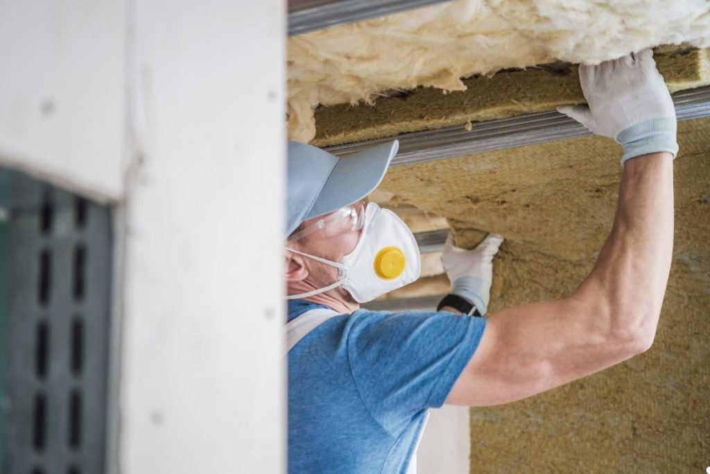 A man in a mask and gloves installs insulation in a building, ensuring safety and proper installation.